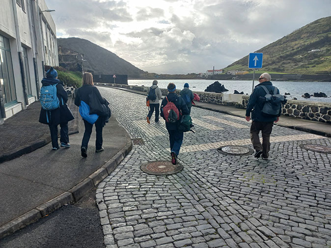 People walking on a cobblestone street with the sea and mountains in the background