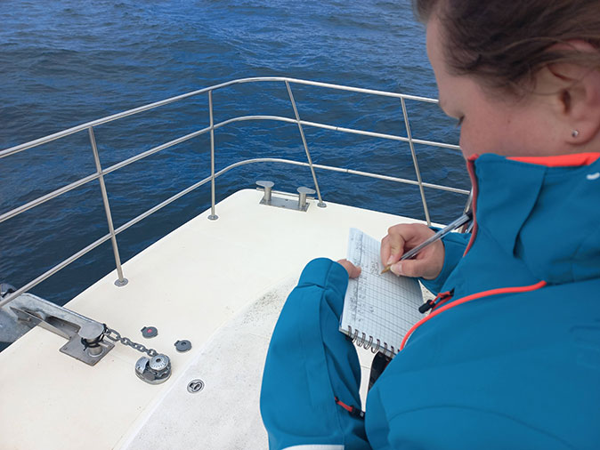 A woman standing on a boat writing something in a notebook