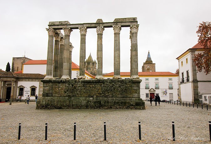 Several pillars, part of a Roman ruin, with white buildings in the background
