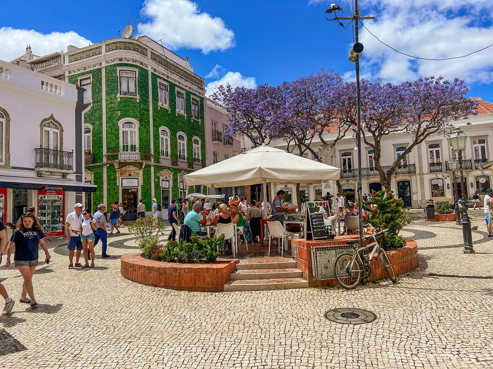 a cobblestone town square with a terrace, several people and historical buildings
