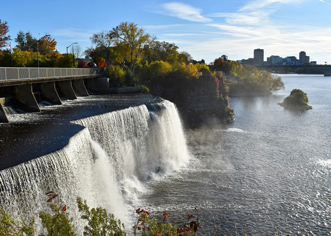 A waterfall surrounded by fall foliage, with highrise buildings in the background