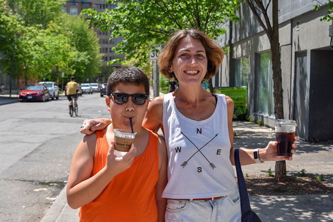 Living in Ottawa, Ontario A woman in a white top holding her arm around her son, in an orange top, both holding a drink, outside surrounded by trees and buildings