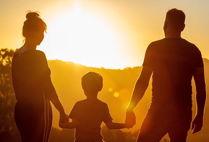 A family holiday in Marbella, Spain A man, a woman and a child holding hands, looking at the sun setting
