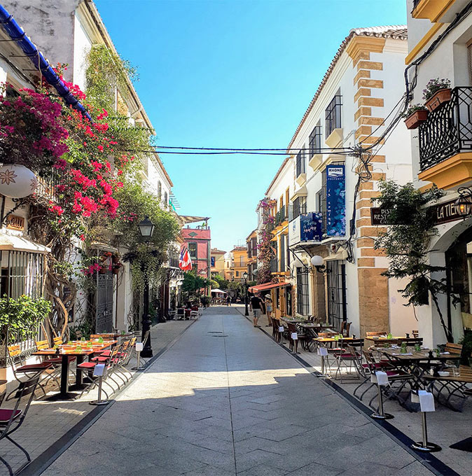 a narrow street with historic buildings on both sides and terraces without people