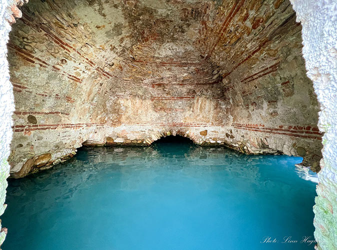 Explore ancient thermal baths with the kids An ancient thermal bath with bright blue water and brown stone walls