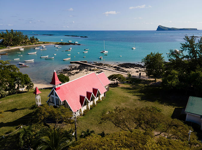 Why move to Mauritius A church with a red roof on a hill overlooking a beautiful bay with bright blue water and several boats