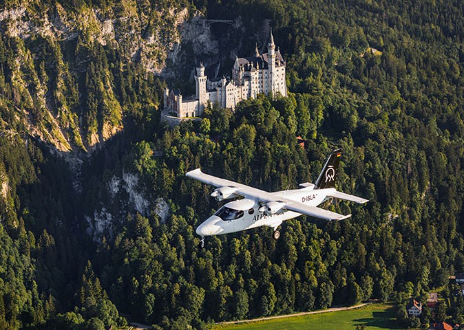 A small plane in the air with a large castle and forest in the background