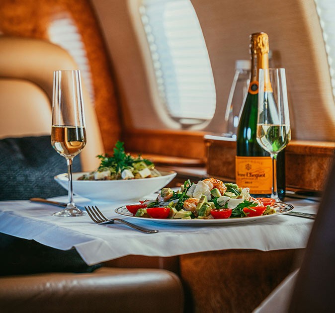 Hiring a private jet to travel in style A table inside a private plane with a bottle of champagne, 2 glasses and 2 plates of food