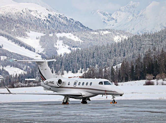 Renting a private jet to go skiing in Switzerland A white jet surrounded by snow covered mountains and pine trees