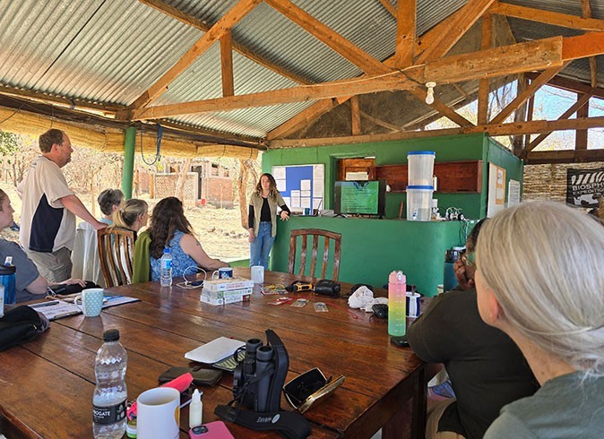 The start of the volunteer project in a wildlife reserve in Malawi A group of people sitting around a wooden table looking at a woman giving a presentation