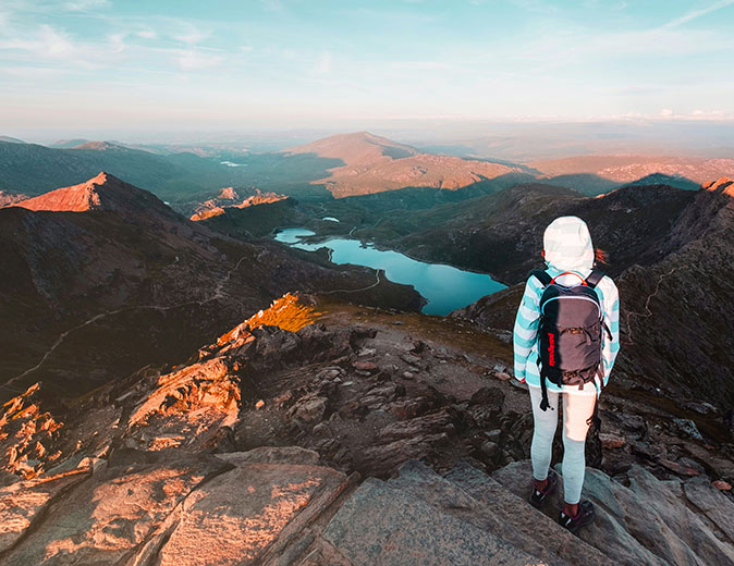 A sunset hike up Snowdon A person with a backpack standing on top of a mountain at sunset