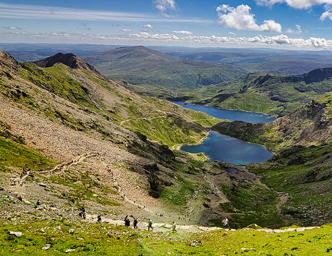 Several people hiking Snowdon Several people on a hiking trail in the mountains with a lake in the background