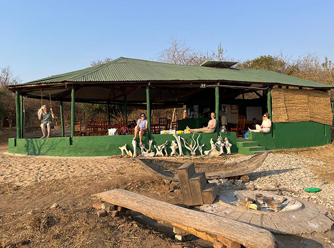 Base camp during the volunteer project in Malawi, Africa A dining area with a green roof, various people, and a fire pit in the foreground