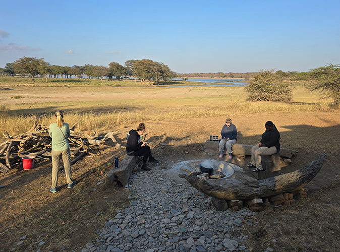 cold mornings while volunteering with elephants in Africa 4 women around a campfire with a lake in the background