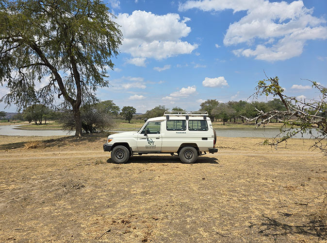 Doing field work as part of the volunteer project in Malawi, Africa A white 4 wheel drive car in a dry African landscape with a lake in the background