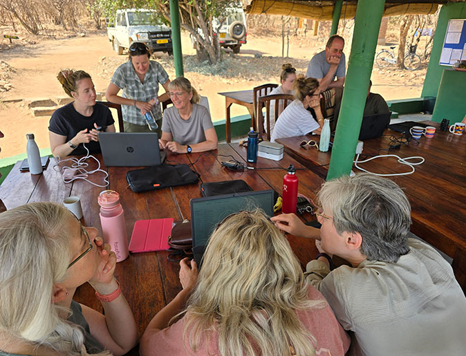 Data entry as part of a volunteer project studying elephants and hippos A group of people sitting at a large table looking at 3 different laptops