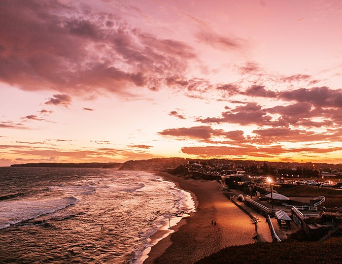 Things to know about time zones in Australia Sunset on the coast with a sandy beach, waves and several buildings