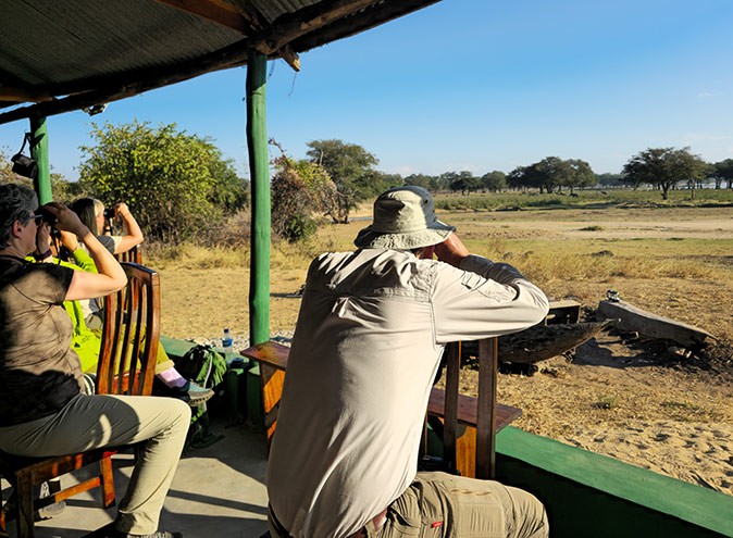 Stydying elephants while volunteering with Biosphere Expeditions 3 people sitting on chairs looking at elephants through binoculars