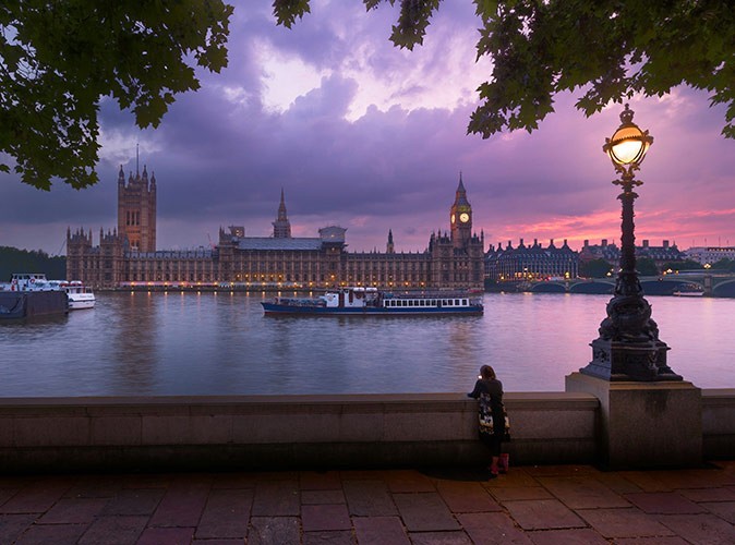 A pink and purple sunset sky above a river with historic buildings in the background