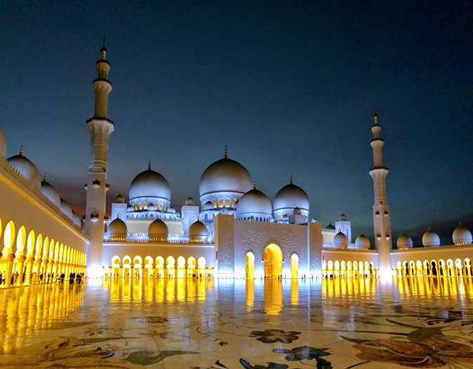 A large white mosque after dark, with yellow lights
