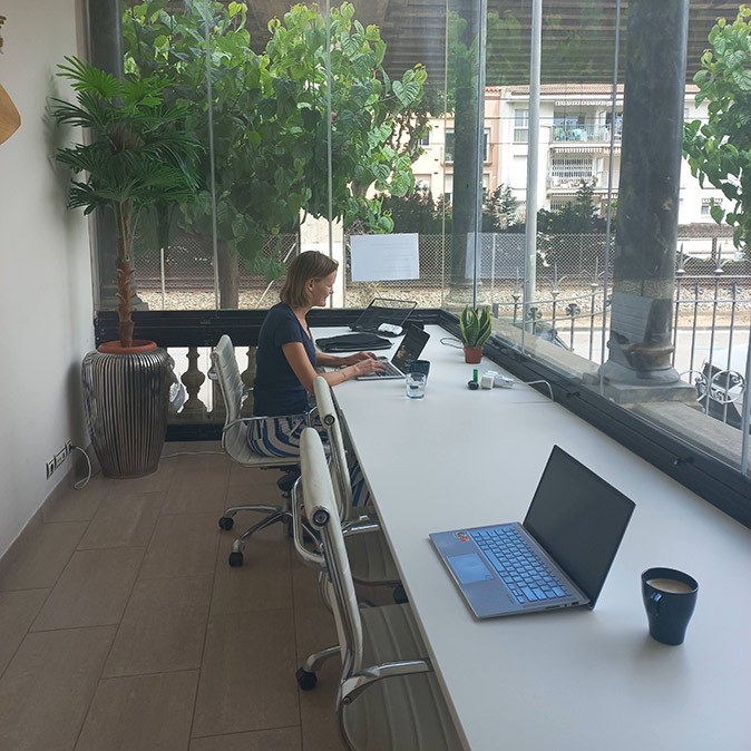 Working fro a coliving space in Spain just outside of Barcelona a woman working on her laptop at a long white table with large windows