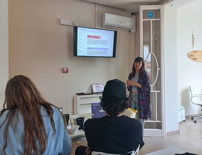 Skill sharing at a coliving space in Spain A woman standing next to a screen sharing a presentation with 2 people sitting at a table