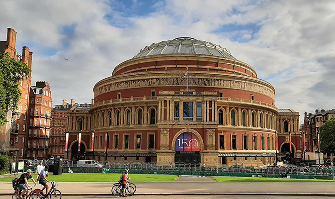 A large building in the shape of a dome with greenery and cyclists in front of it