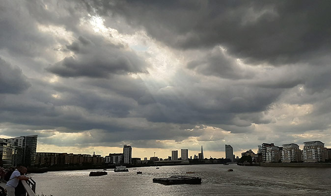 Gray clouds over a wide river with boats and highrise buildings in the background