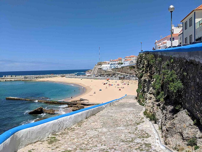 A more laid-back destination for digital nomads in Portugal A walkway leading to a sandy beach with some rocks in the foreground and a town in the background
