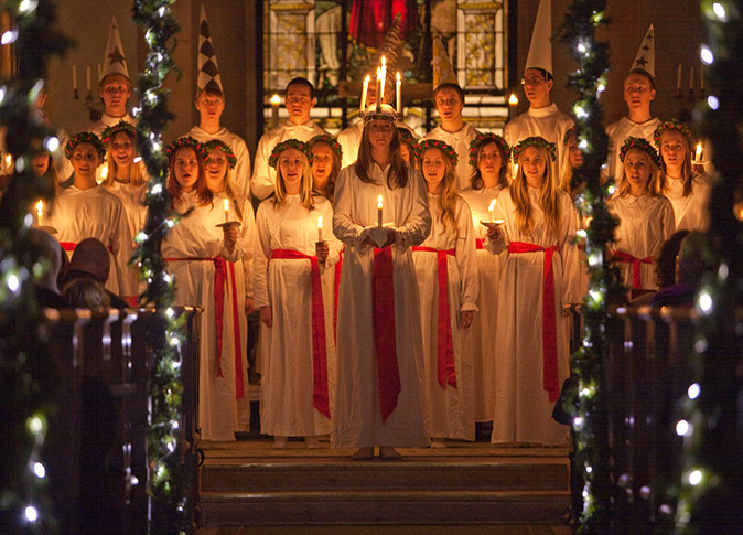 A Christmas tradition in Sweden A group of young people on a stage, wearing white robes and holding candles