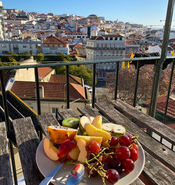 Where to live in Lisbon A plate with fruit on a small wooden table on a balcony overlooking a city