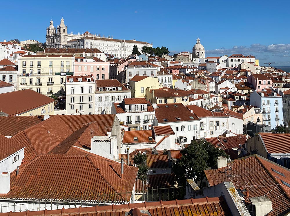 Aerial view of Lisbon, showing red roofs, white houses and a large cathedral in the background