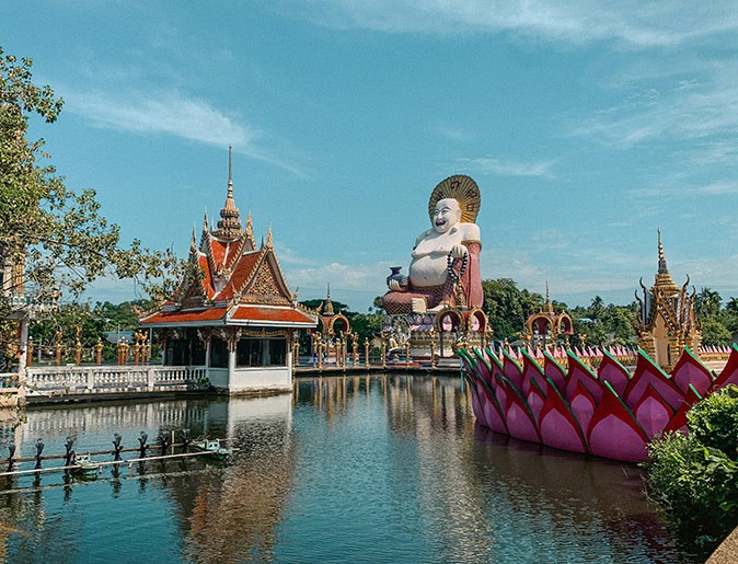 One of the sights to see in Koh Samui A Buddha statue and a temple next to a body of water