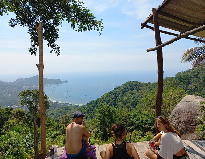 Koh Tao and Koh Samui have a different vibe 3 people sitting on a platform overlooking a lush green landscape with the sea in the background
