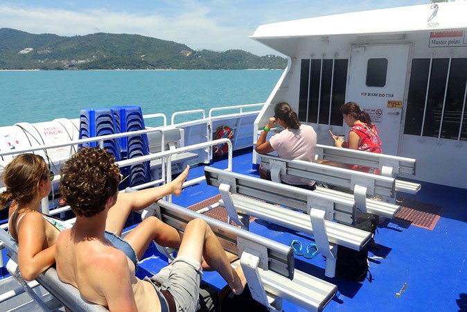 Going to Koh Tao or Koh Samui 4 people sitting on white benches on an open-air ferry with an island in the background