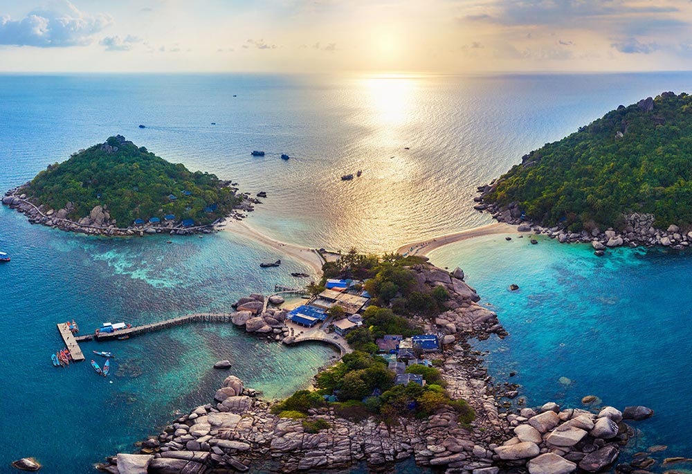 Aerial view of 3 island with greenery and rocks, connected by small stretches of beach