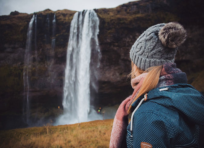 RV road trip in Iceland A girl with a gray woolly hat and blue jacket looking at a large waterfall