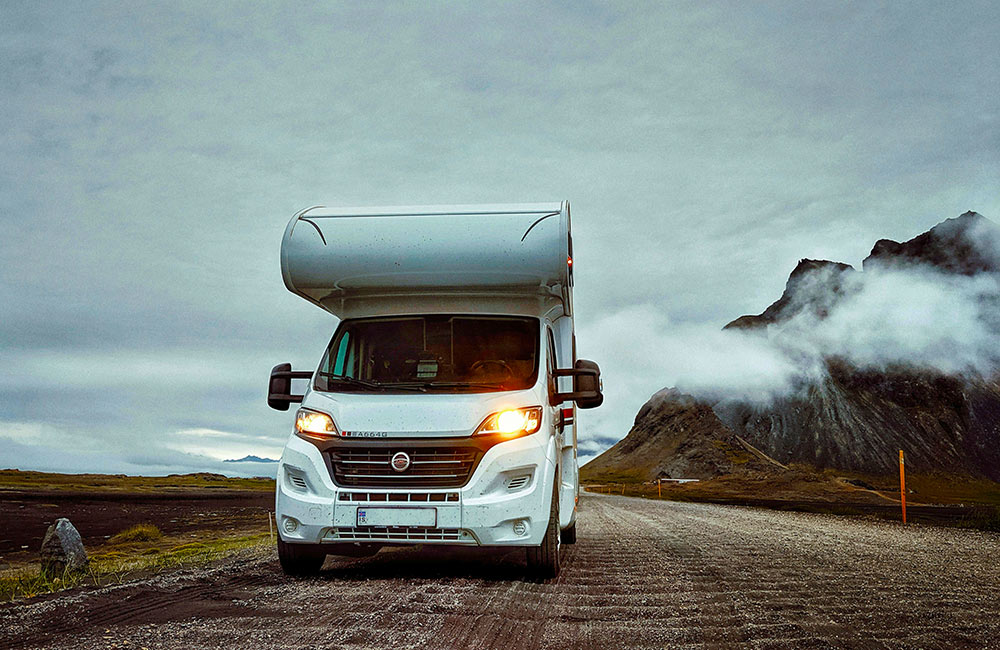 A white campervan on a brown road with mountains covered in clouds in the background