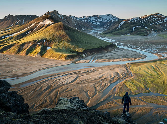Camping in Iceland Aerial view of a brown and green landscape with mountains in the background and a small silhouette of a man