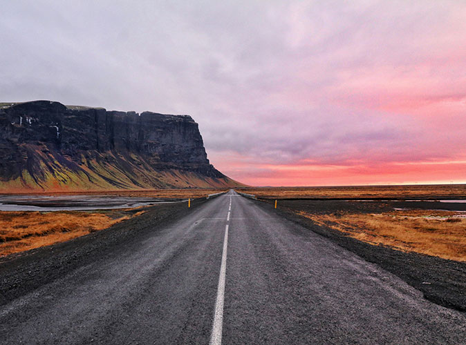 Renting a campervan in Iceland A wide tarmac road with a red sky and large mountain in the background