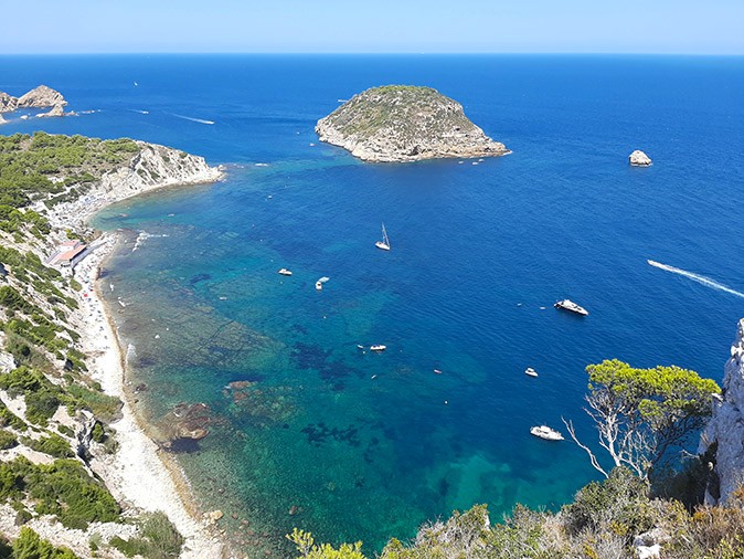 Chartering a yacht in Spain A bay with several boats, bright blue water, a beach and a small rocky island just off the coast