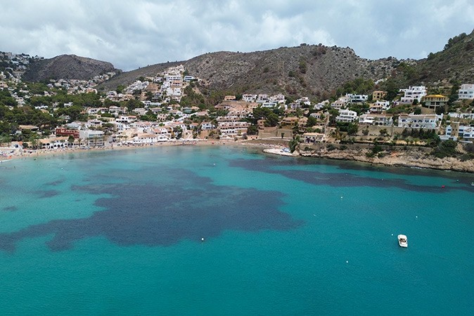 Renting a boat in Spain A bay with clear blue water with a beach, some houses and mountains in the background