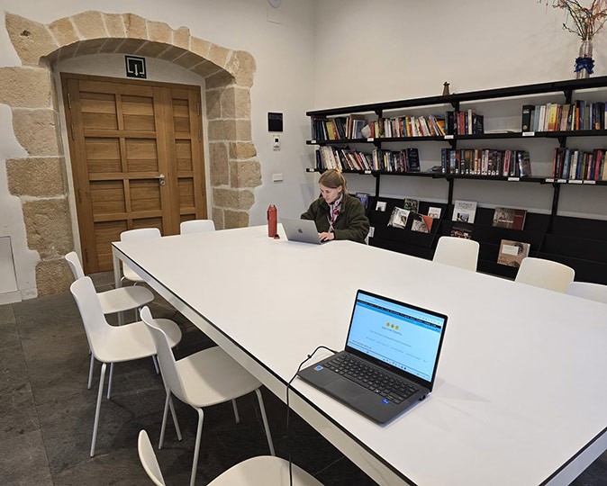 Working remotely on the Camino de Santiago A large white table with white chairs with a blond woman working on a laptop at one end, and a laptop with an empty seat on the other end