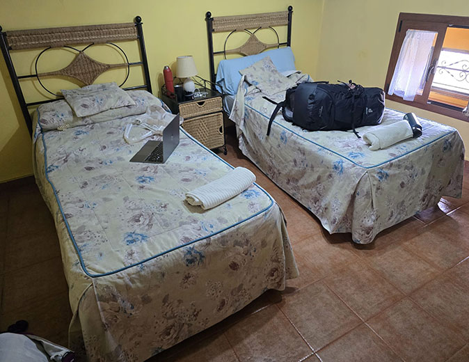 A hostal along the Camino de Santiago 2 single beds with towels, a laptop and a backpack, in a tiled room with yellow walls