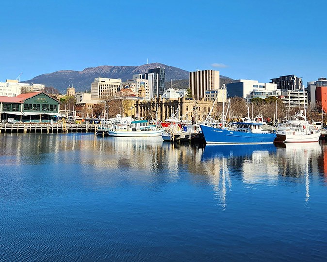 A harbour with various boats, blue water and buildings and mountains in the background