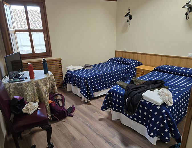 Staying in an albergue on the Camino de Santiago 2 single beds with blue covers, a small window and a table