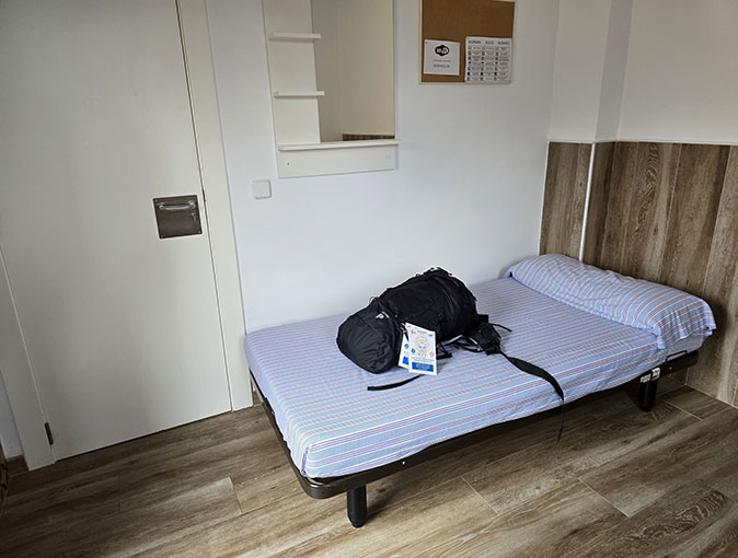 Different accommodation options on the Camino de Santiago A simple single bed with a backpack on top of it inside a sparsely decorated room