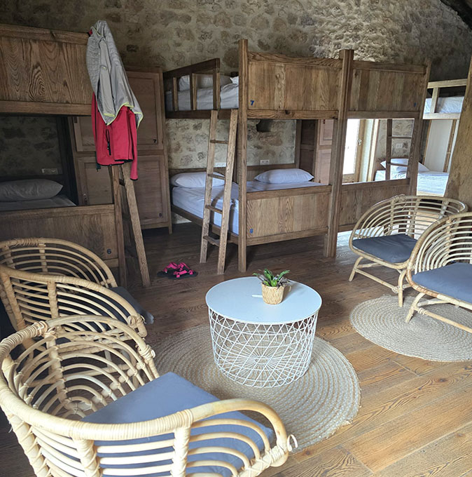 Comfortable accommodation on the Camino de Santiago A room with several bunk beds with wooden frames, plus 4 comfortable wooden chairs and a side table