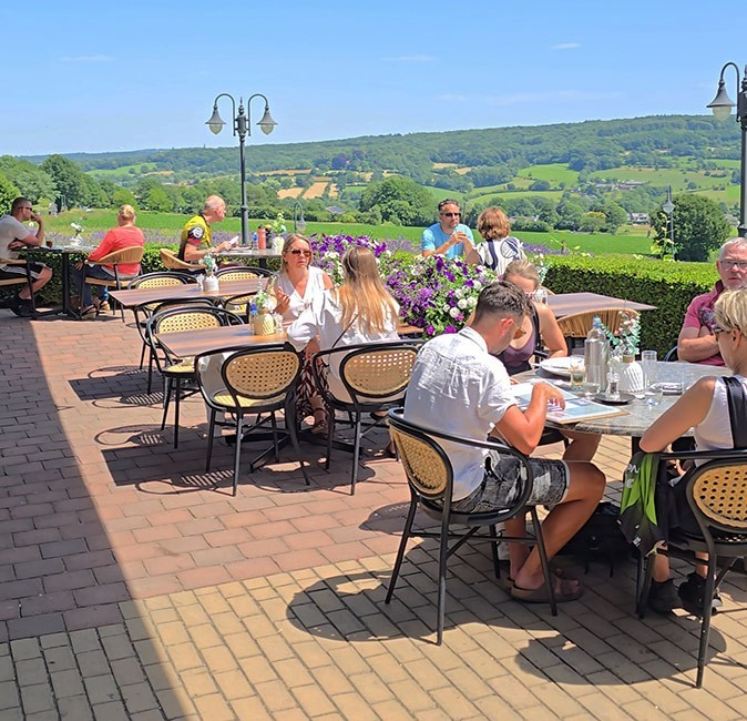 Several people on a sunny terrace overlooking a green, rolling landscape