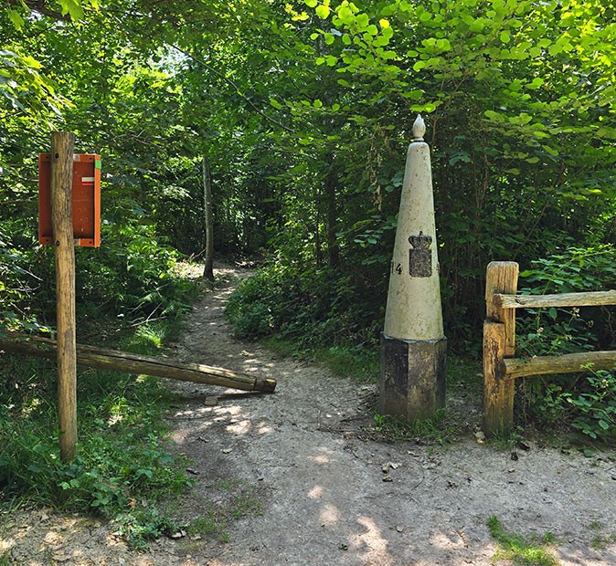 A wooded trail with a fence and a large pole indicating a border crossing